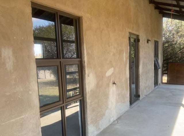 Dark bronze-framed aluminium windows and door along a covered porch of a rustic home