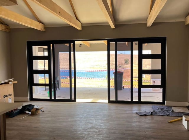 Large black-framed aluminium sliding glass doors installed in a home under renovation